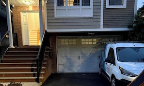 A two-story house with a garage, a white van parked in front, and a staircase leading to the front door.