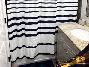 Un baño con cortina de ducha a rayas, lavabo con encimera de granito y un armario.