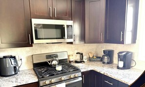 A kitchen with a stove, microwave, coffee maker, and tea kettle.