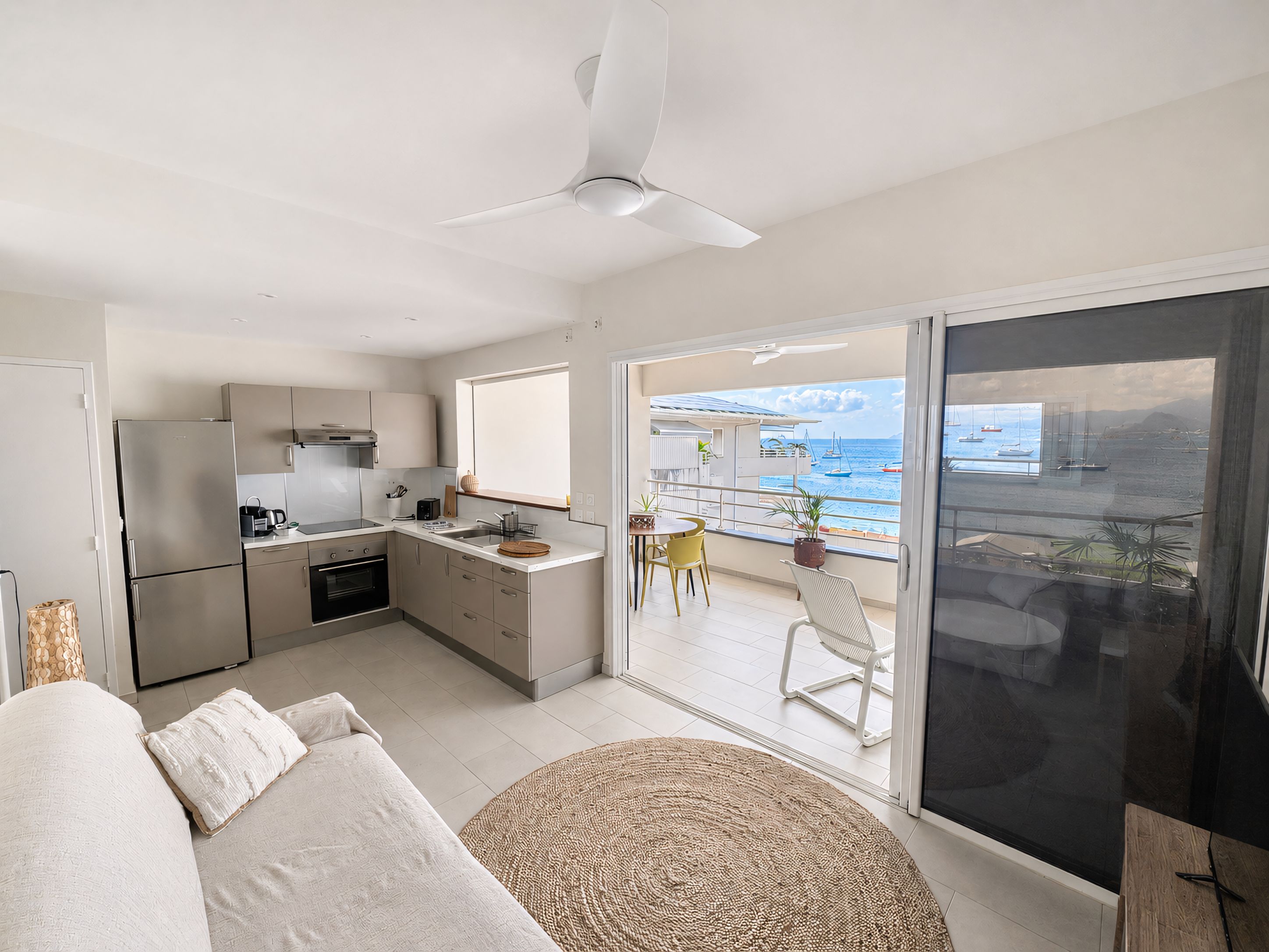 A modern kitchen with a dining area, a sofa, and a view of the sea.