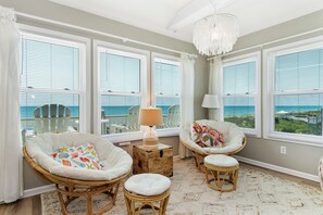 A room with large windows, wicker furniture, a lamp, and a chandelier. - Oceanfront Condo w/ Panoramic Views, Whirlpool Tub & Beach Access (Emerald Isle)