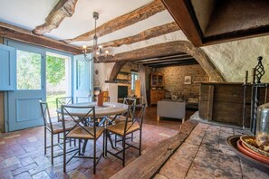 Ein rustikales Interieur mit freiliegenden Holzbalken, einer Steinwand, einem runden Tisch mit Stühlen und einem Kamin.