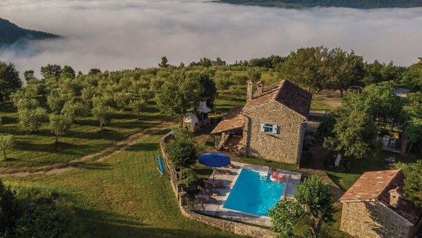 A stone house with a swimming pool, surrounded by trees and a view of a valley. - Casa Biloslavi with pool (Groznjan)