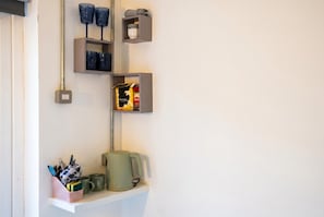 A kitchen area with a coffee maker, mugs, and utensils on a shelf. - Cosy Tiny Home for 2 with Garden · Walk to Filey Beach (North Yorkshire)