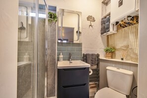 Un baño con cabina de ducha de vidrio, lavabo con espejo, inodoro y toallero con toallas.