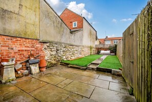 Un patio con suelo de piedra, pared de ladrillo, pared de piedra y cerca de madera.