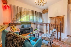 Una sala de estar con sofá, sillón, televisión y un balcón con baranda de madera.