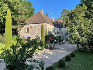 A stone building with a sloped roof, surrounded by a gravel driveway and lush greenery. - Suite La Denise in the Heart of the Vineyards (Curtil-Vergy)