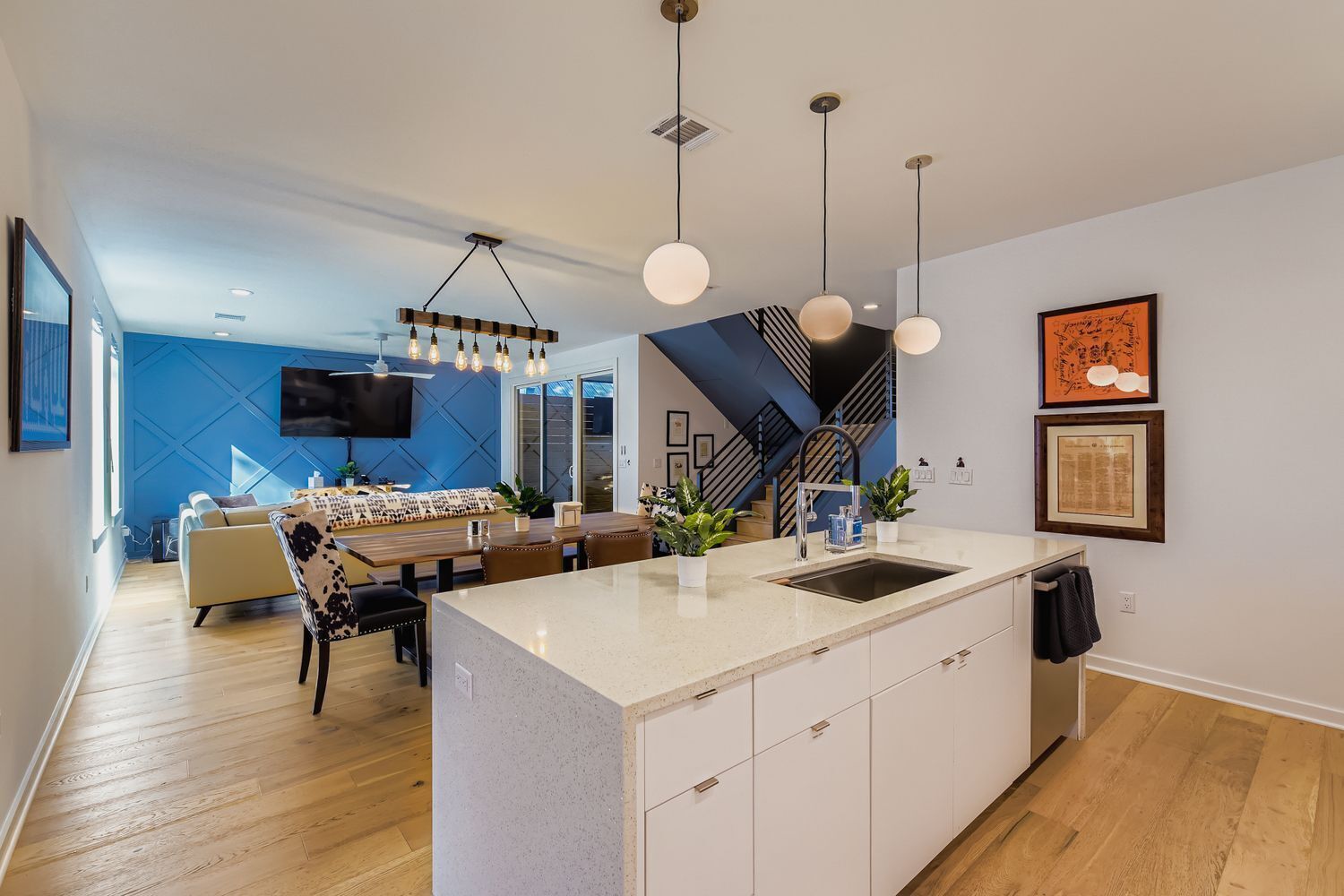 Cozinha moderna com ilha central, iluminação pendente e área de jantar com sofá e mesa.