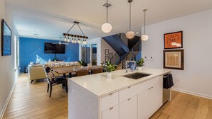 A modern kitchen with a central island, pendant lighting, and a dining area with a sofa and table. - 4 BR Home, Hot Tub, Cowboy CHILL Pool, Private Deck/Pergola, 3-minutes to Downtown Austin! (Austin)