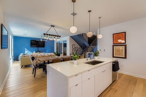 Eine moderne Küche mit einer zentralen Kochinsel, Pendelleuchten und einem Essbereich mit Sofa und Tisch.