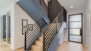 A modern staircase with black railings, wooden steps, and a glass door at the top. - 4 BR Home, Hot Tub, Cowboy CHILL Pool, Private Deck/Pergola, 3-minutes to Downtown Austin! (Austin)