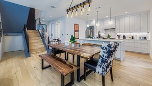A modern kitchen with a wooden dining table, bench seating, pendant lighting, and a staircase. - 4 BR Home, Hot Tub, Cowboy CHILL Pool, Private Deck/Pergola, 3-minutes to Downtown Austin! (Austin)