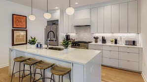 A modern kitchen with a central island, bar stools, stainless steel appliances, and pendant lighting. - 4 BR Home, Hot Tub, Cowboy CHILL Pool, Private Deck/Pergola, 3-minutes to Downtown Austin! (Austin)