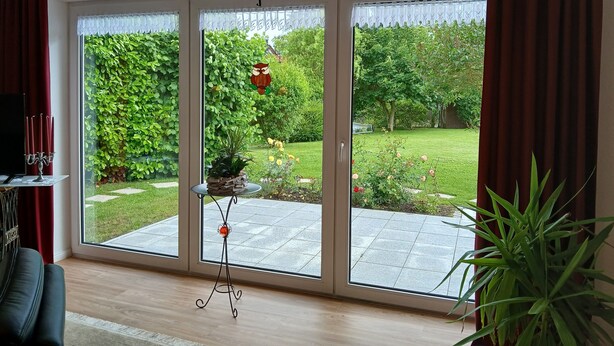 A room with a large sliding glass door leading to a garden, a small table with a decorative item, and a television on a stand. - Ground-Level Holiday Home by the Salt Marshes (Sande)