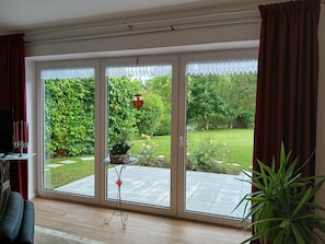 Ein Zimmer mit einer großen Schiebeglasdoor zum Garten, einem kleinen Tisch mit einem dekorativen Gegenstand und einem Fernseher auf einem Schrank.