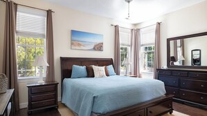 Quarto com cama grande, penteadeira, mesa de cabeceira, luminária, quadro e janela com cortinas.