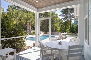 A covered outdoor area with a pool, white furniture, and a view of the surrounding greenery. - Blue Byrds - 4 Bedroom Home (Emerald Isle)
