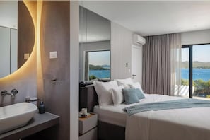 Ein modernes Hotelzimmer mit einem großen Bett, einem Nachttisch, einer integrierten Spüle und einem großen Fenster mit Meerblick.