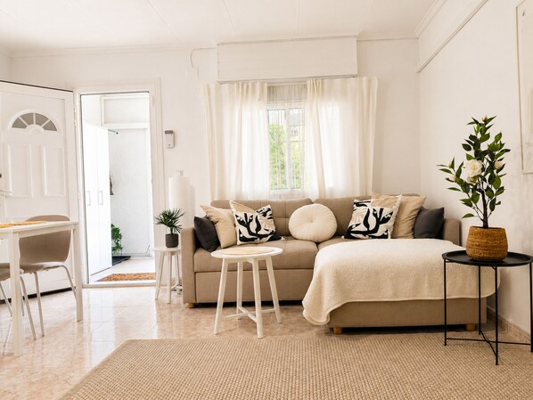 Ein modernes Wohnzimmer mit einer Couch, einem kleinen runden Tisch, einem Sessel und einer Topfpflanze.