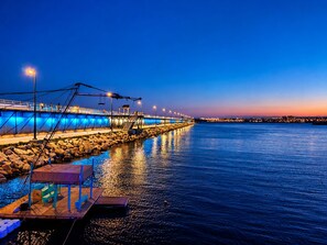 Eine Uferpromenade mit einem hölzernen Steg, Steinstufen und einer Brücke im Hintergrund.