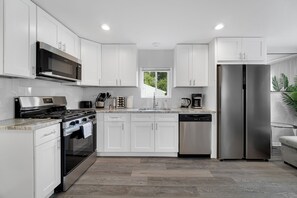 Een moderne keuken met witte kasten, roestvrijstalen apparatuur en een raam dat voor natuurlijk licht zorgt.