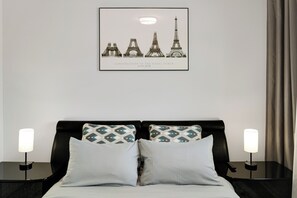 Een hotelkamer met een bed, twee nachtkastjes, een lijst met een foto van de Eiffeltoren en een raam met gordijnen.