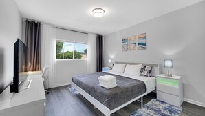 A modern hotel room with a bed, bedside tables, a TV, and a window with curtains. - Bright & Modern 2-Story Near Northwestern (Evanston)
