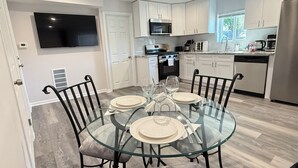 A modern kitchen with white cabinets, a stainless steel refrigerator, and a dining area with a glass table and chairs. - Bright & Modern 2-Story Near Northwestern (Evanston)