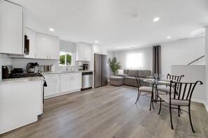 A modern kitchen with white cabinets, a dining area with a glass table and metal chairs, and a wooden floor. - Bright & Modern 2-Story Near Northwestern (Evanston)