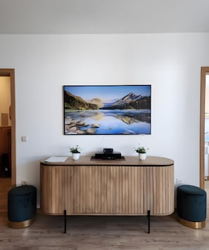 Un taulell de recepció modern amb un gran quadre de paisatge penjat a la part superior, dues plantes en testos i un televisor de pantalla plana.