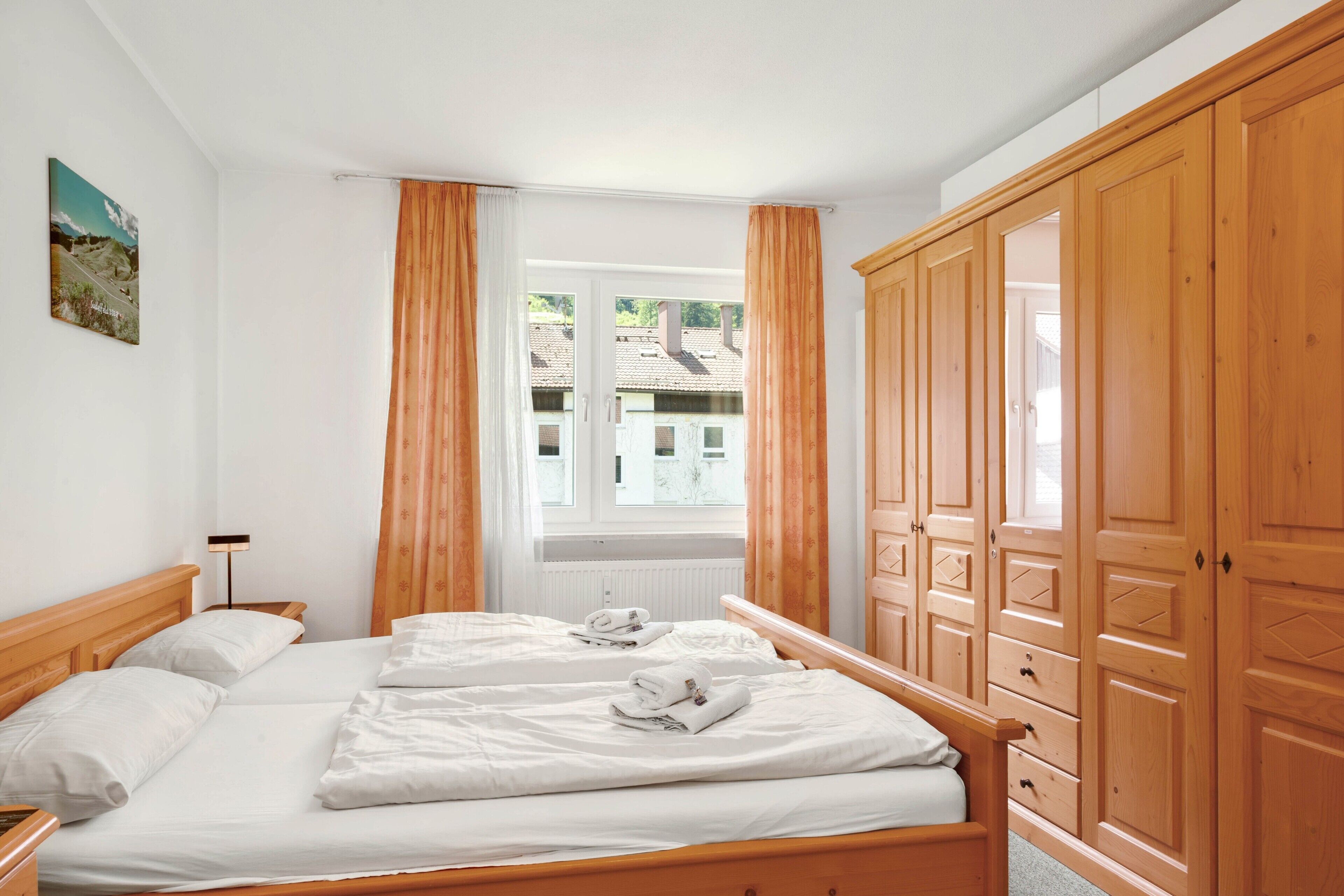 Ein Doppelbett mit weißer Bettwäsche, ein Holzschrank und ein Fenster mit Vorhängen.