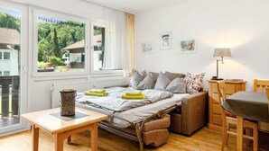 Ein Schlafzimmer mit Bett, Tisch, Stuhl, Lampe und Fenster mit Blick ins Grüne.