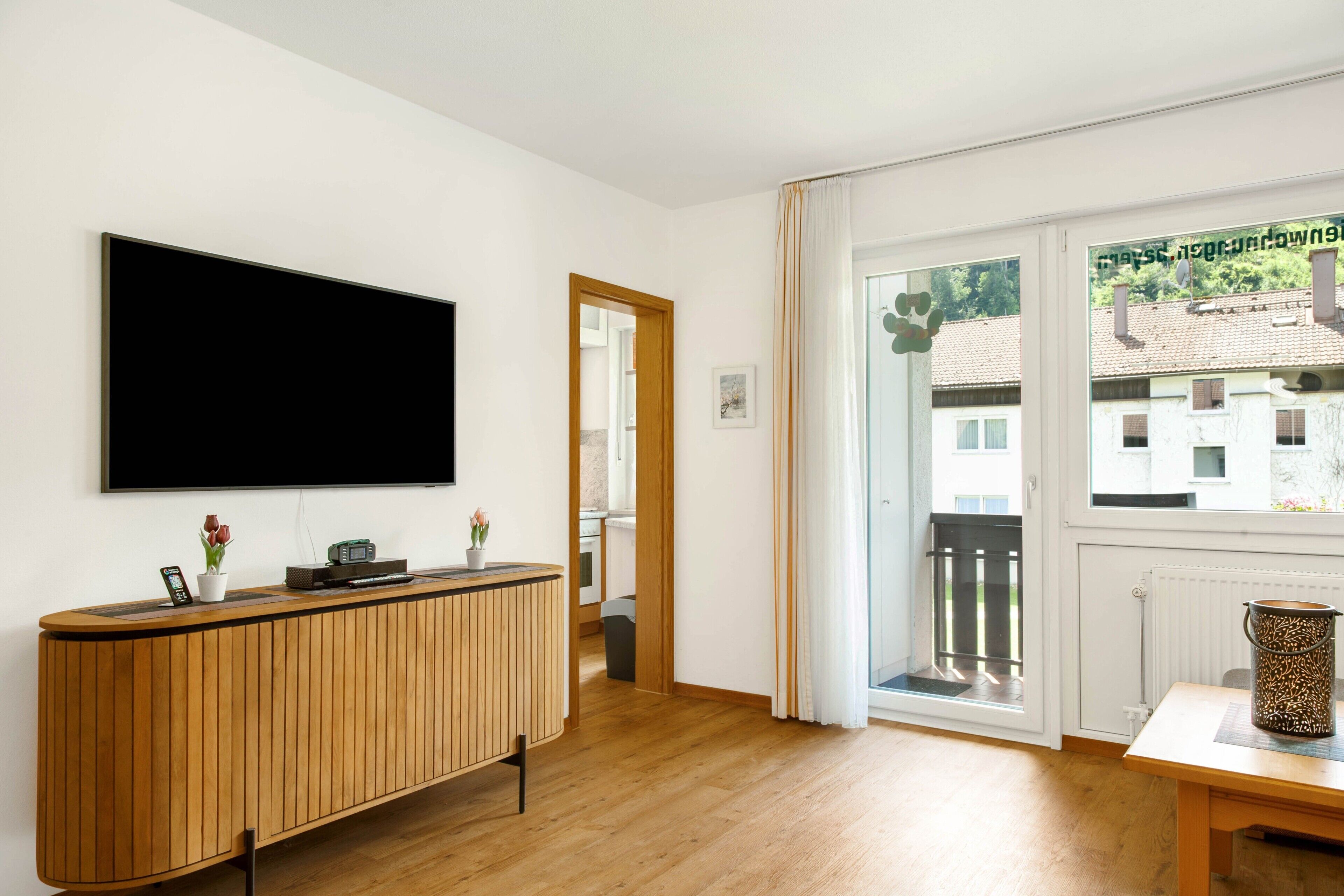 Una sala de estar moderna con un televisor de pantalla plana grande, muebles de madera y vistas a edificios a través de un amplio ventanal.