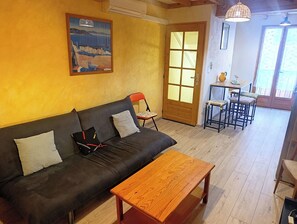 En hyggelig stue med en sofa, et træbord, et spiseområde med bord og stole, samt et stort vindue med udsigt.
