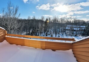 Eine Holzterrasse mit Blick auf einen verschneiten Wald und einen klaren Himmel.