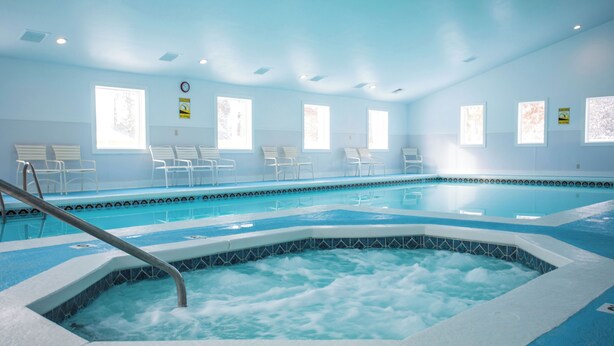 Un'ampia piscina interna con una vasca idromassaggio al centro, circondata da sedie e panche bianche.