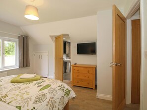 A bedroom with a bed, a dresser, a television, and a bathroom visible through an open door. - Westington Hall (Leominster)