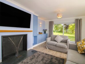 A living room with a flat-screen TV, a fireplace, a sofa, and a view of a garden. - Westington Hall (Leominster)