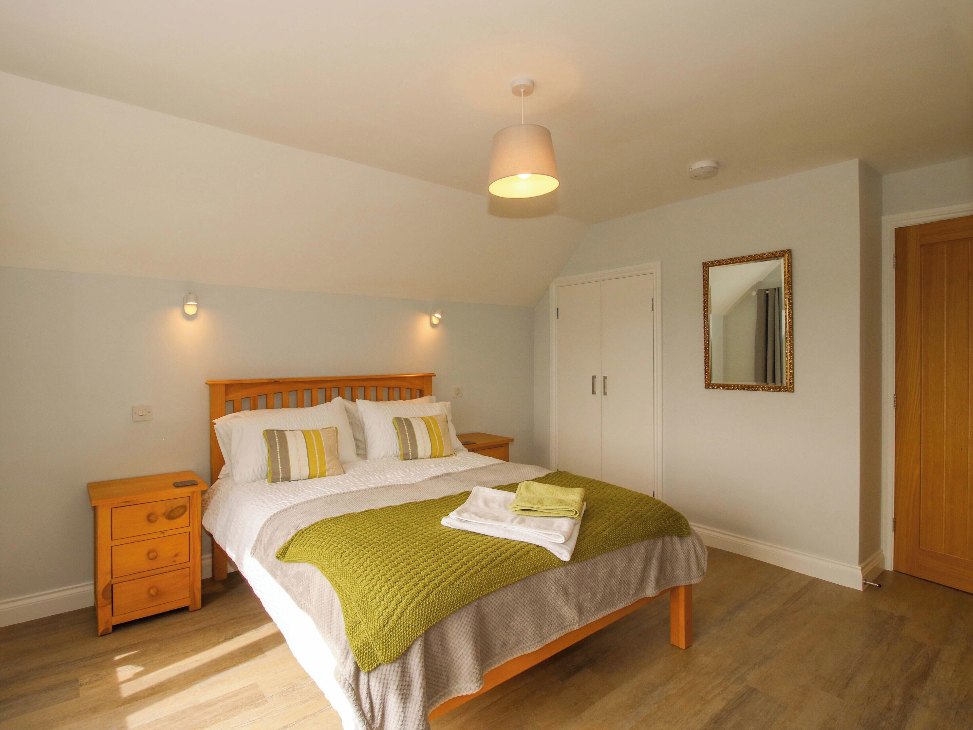 A bedroom with a wooden bed, bedside tables, a wardrobe, a mirror, and a hanging light fixture.