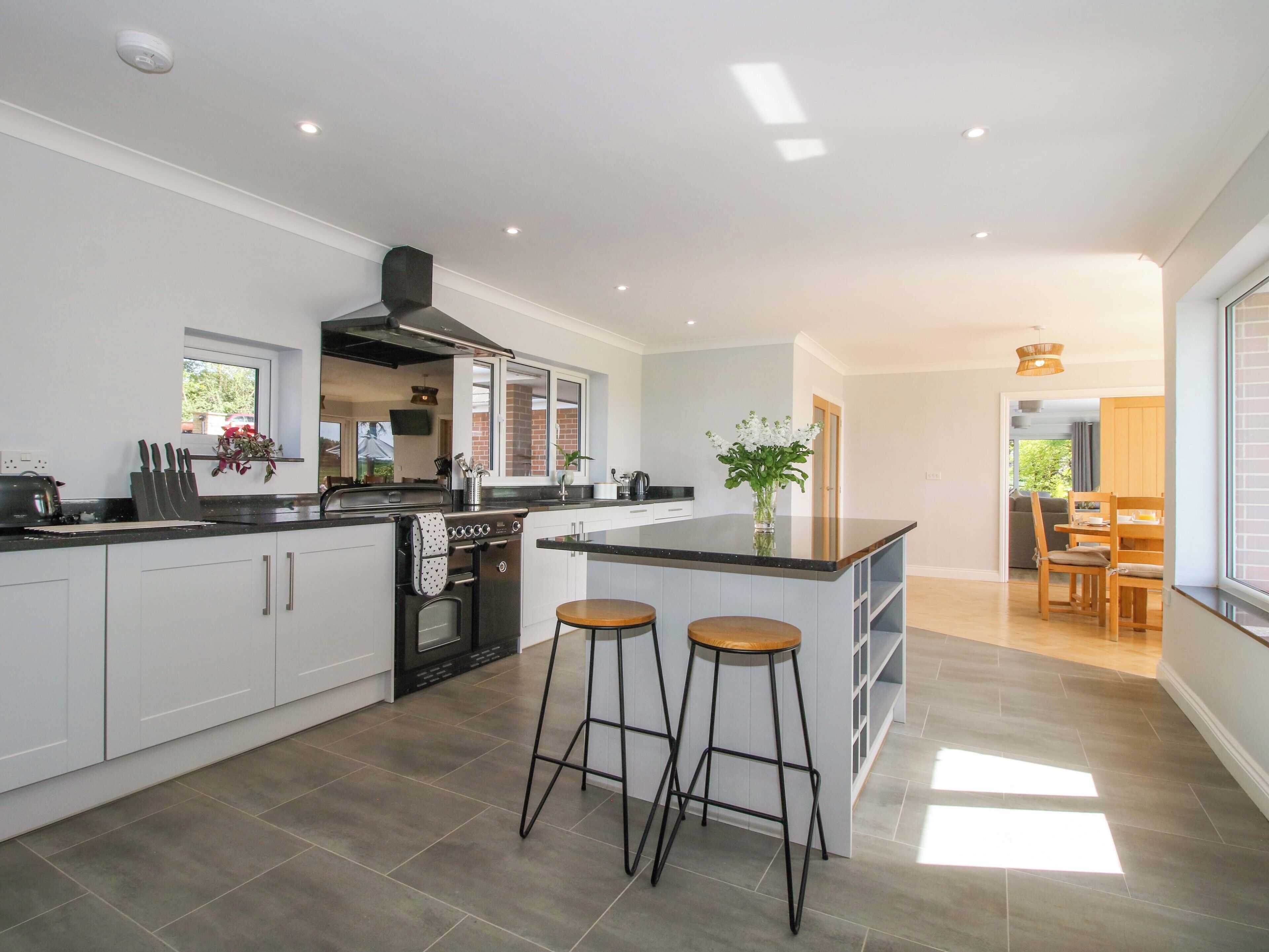 A modern kitchen with a central island, bar stools, a stove, and a window overlooking the garden.