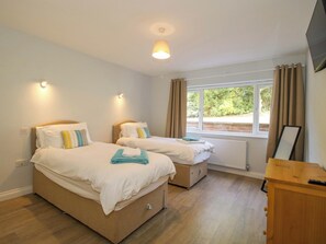Ein Schlafzimmer mit zwei Betten, einem Holzschrank, einem Fenster mit Vorhängen und einer Deckenleuchte.