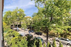 Straßenansicht mit parkenden Autos, Bäumen und Gebäuden.