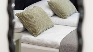 Ein Bett mit Kissen und einer Steude, ein schwarzer Kopfteil und ein Spiegel, der den Raum widerspiegelt.