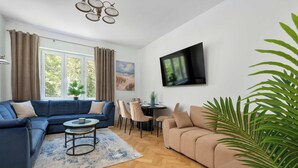 Ein Wohnzimmer mit Ecksofa, Couchtisch, Wand-Fernseher und Essbereich mit Stühlen und Tisch.