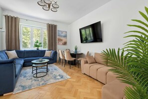 Ein Wohnzimmer mit Ecksofa, Couchtisch, Wand-Fernseher und Essbereich mit Stühlen und Tisch.