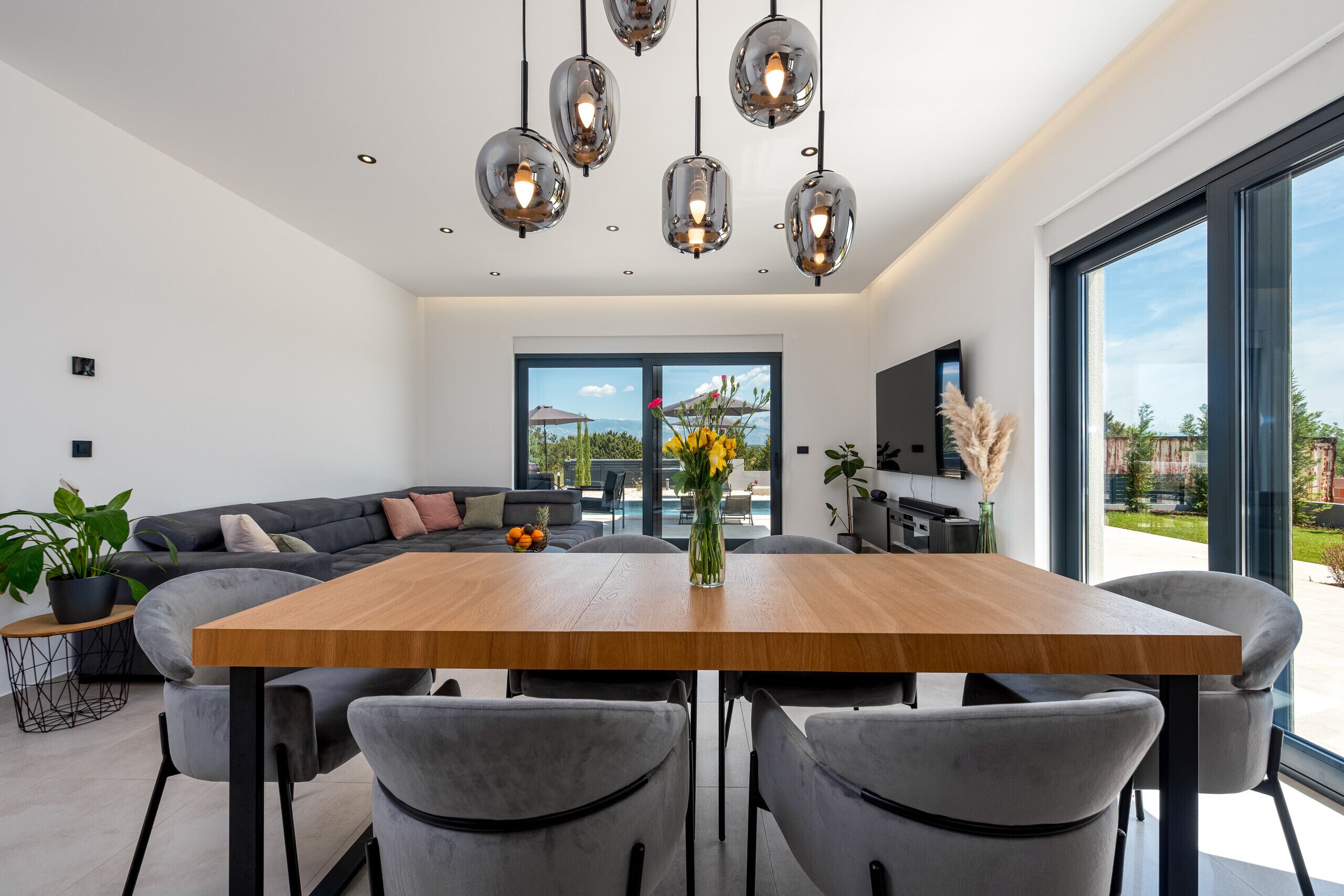 Un intérieur moderne avec une table à manger en bois, des chaises à revêtement gris et des luminaires suspendus.
