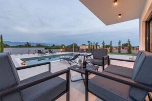 An outdoor pool area with lounge chairs, a table with a bottle and glasses, and a view of mountains in the background. - Villa Enija Zadarvillas (Nin)