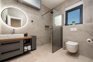 A modern bathroom with a glass shower enclosure, a toilet, a sink with a mirror, and a window with a view. - Villa Enija Zadarvillas (Nin)