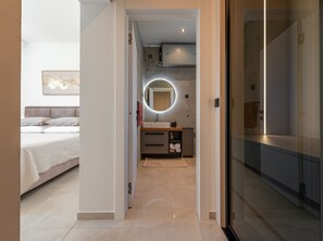 Ein modernes Schlafzimmer mit Bett, ein Badezimmer mit Spiegel und eine Glastür zu einem Flur.
